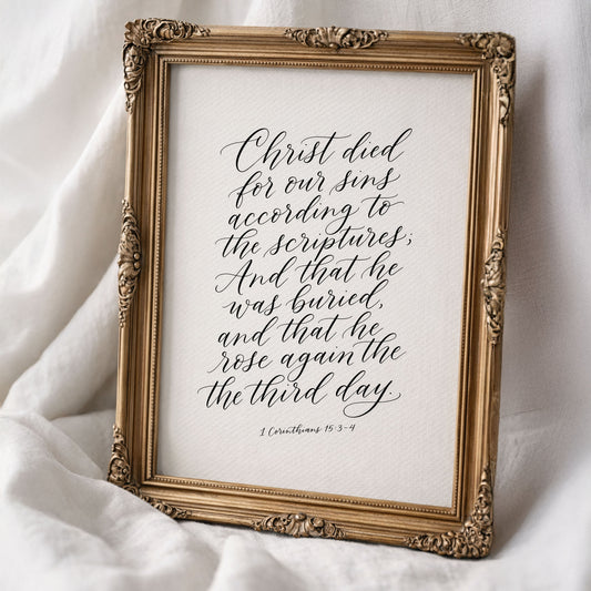 a framed print with a hand-lettered Bible verse, specifically from 1 Corinthians 15:3-4, which reads: "Christ died for our sins according to the Scriptures, and that he was buried, and that he rose again the third day."
