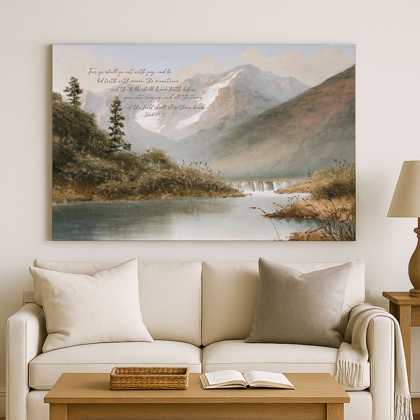 a serene landscape with a mountain range, a river, and lush greenery. The painting is hung on a wall above a white sofa, which has a basket on it. The sofa is positioned in front of a coffee table, and there is a lamp on the side. The overall scene is peaceful and inviting, with the natural elements complementing the comfortable seating arrangement.