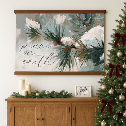 a large painting of a pine tree with snow on its branches, hanging on a wall above a wooden cabinet. The painting has a decorative border and the phrase "Peace on earth" written on it. The cabinet has a small picture frame and some candles on it, creating a cozy and festive atmosphere.