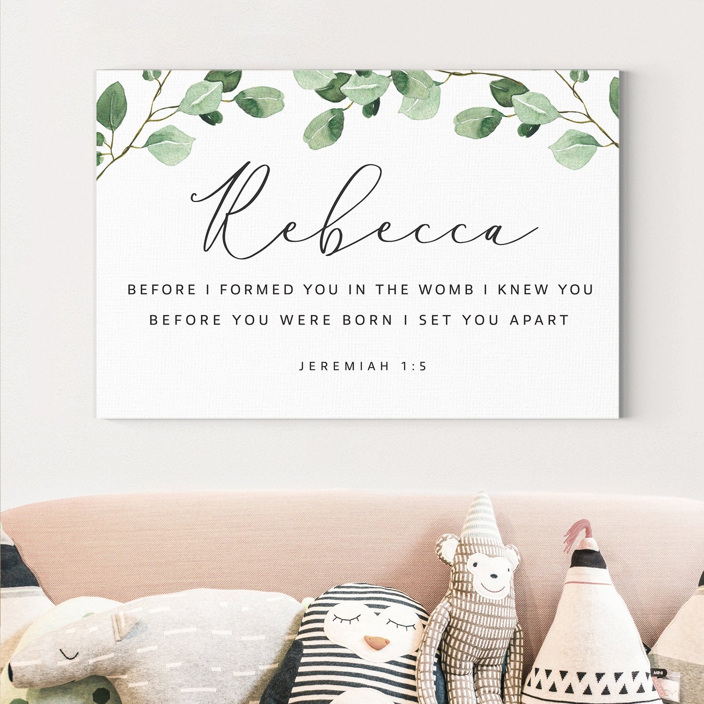 a white wall with a framed Bible verse and a decorative arrangement of stuffed animals on a couch.
