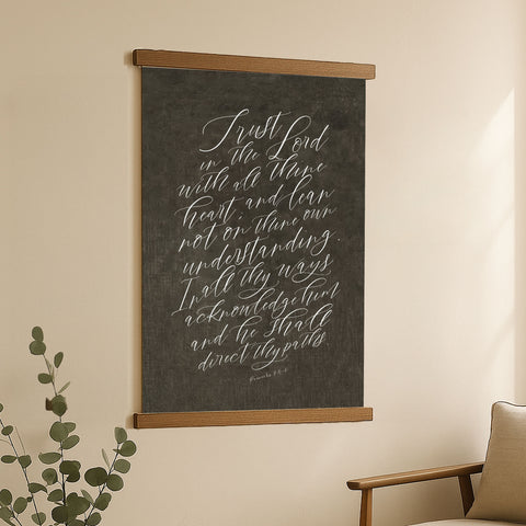 a blackboard with white handwritten text, hanging on a wall next to a plant.