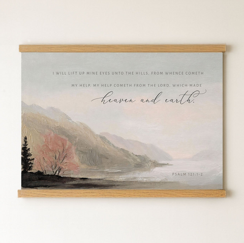 The image is a framed painting depicting a serene landscape with mountains, trees, and a body of water. The painting is mounted on a wall and features a Bible verse from Psalm 121:1-2.