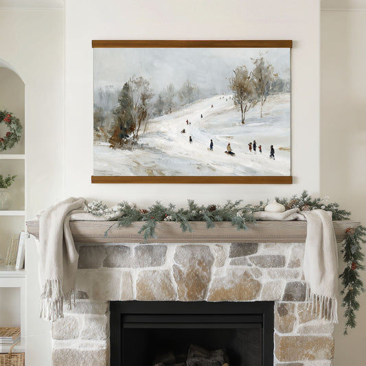 a cozy fireplace decorated for the holiday season, with a painting of a snowy landscape hanging above it. The fireplace is adorned with greenery and a white blanket, creating a warm and inviting atmosphere.