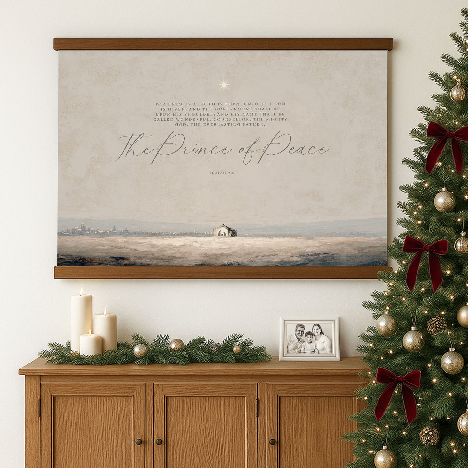 a wooden cabinet with a framed photograph of a family, a Christmas tree decorated with red bows, and a large framed poster of a landscape with a small house and a star in the sky.