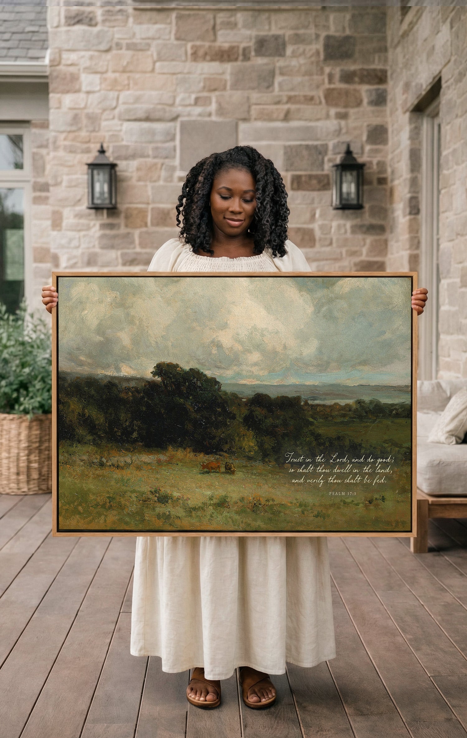 A woman in a white dress holds a large painting of a pastoral landscape, with a quote from the Bible visible on the painting.