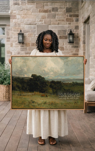 A woman in a white dress holds a large painting of a pastoral landscape, with a quote from the Bible visible on the painting.