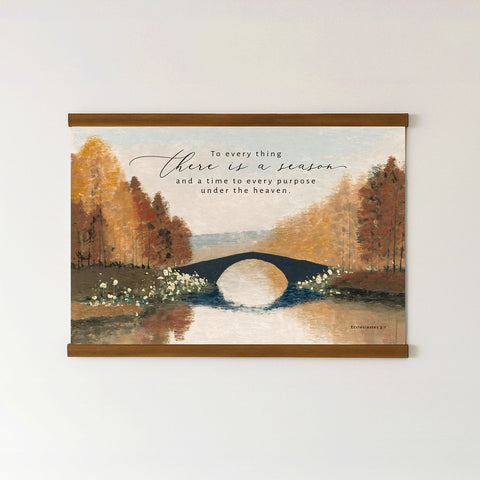 The image is a framed painting depicting a serene landscape with a bridge over a river, surrounded by trees with autumn foliage. The painting is mounted on a wall, and there is a quote in the top right corner that reads, 