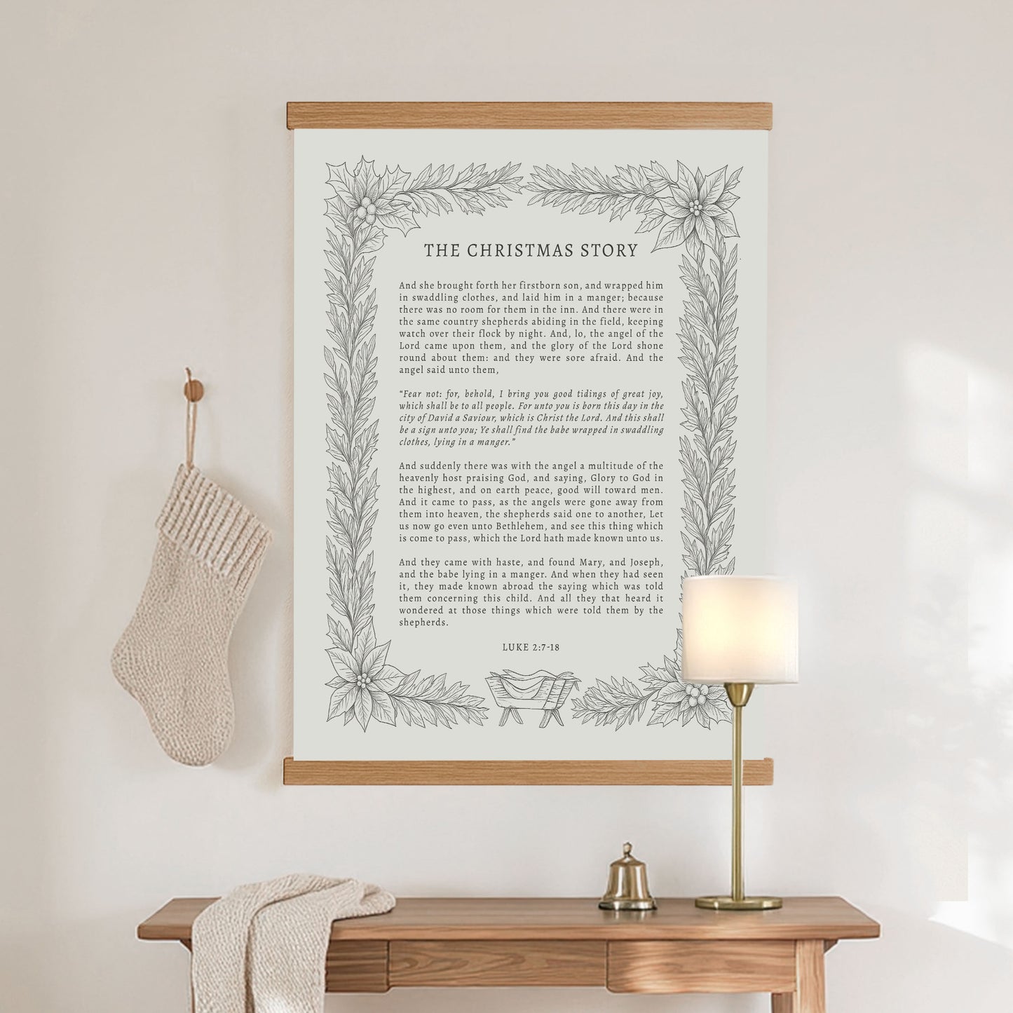 a wooden table with a lamp, a white stocking, and a framed text titled "THE CHRISTMAS STORY" hanging on the wall above it.