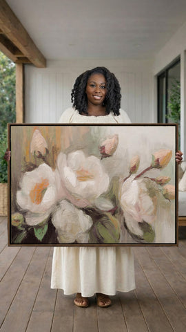 A woman in a white dress holds a large painting of white flowers in a wooden porch.