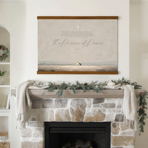 a fireplace mantel decorated with a wreath, pine cones, and a white candle, with a framed Bible verse displayed above it.