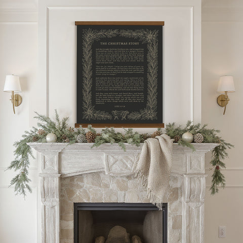 a fireplace decorated with greenery, pine cones, and ornaments, with a framed black and white poster of a Christmas story hanging above it.