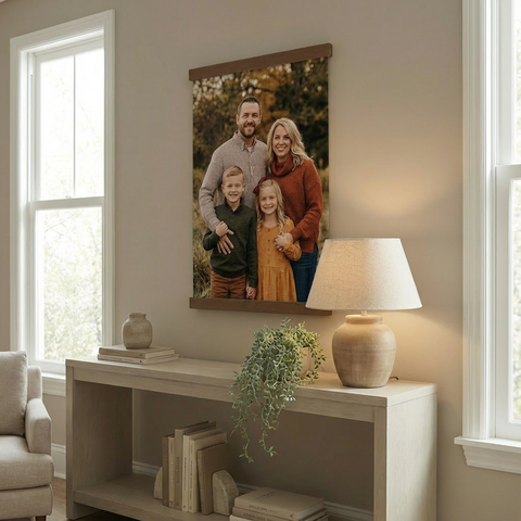 a family portrait hanging on a wall, with a lamp and a plant on a table below it.