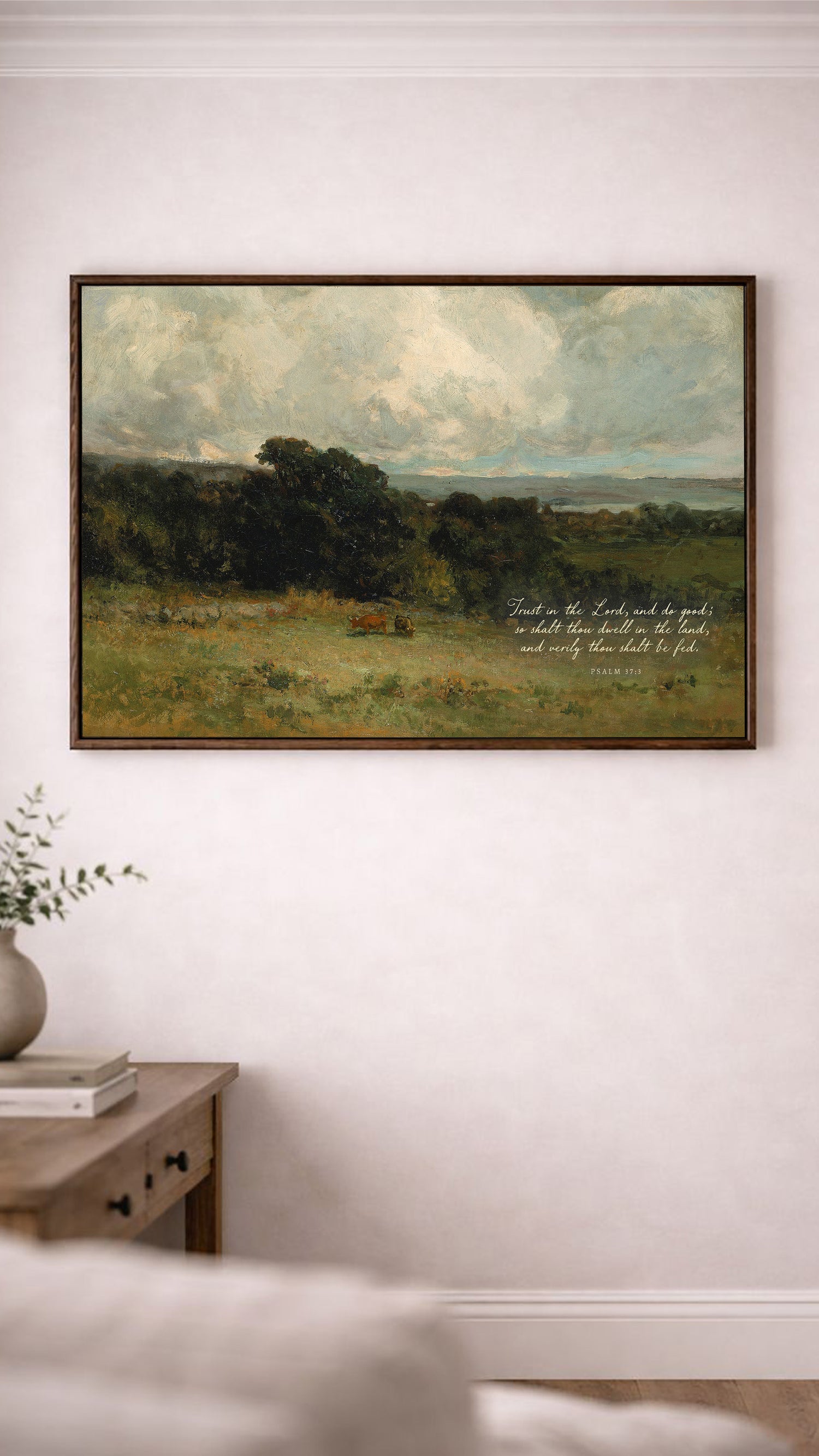a large landscape painting hanging on a white wall, depicting a serene countryside scene with rolling hills, trees, and a cloudy sky.