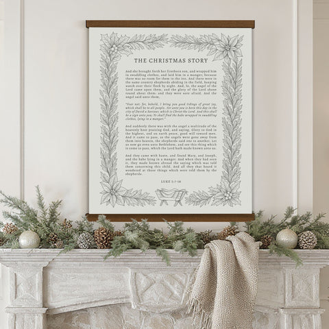 a framed Christmas-themed poster with a wreath and pine cones on a white fireplace mantel.