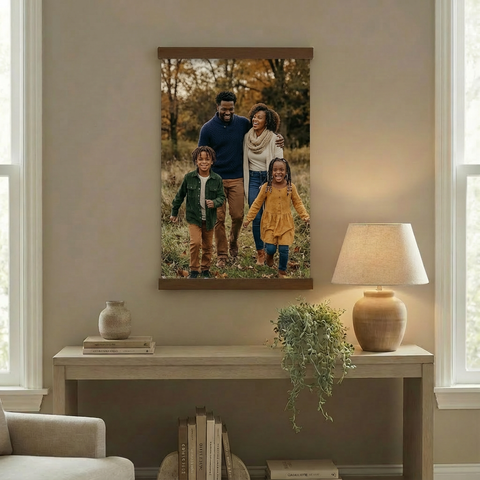a family portrait hanging on a wall, with a wooden console table below it. The table has a lamp and a plant on it.