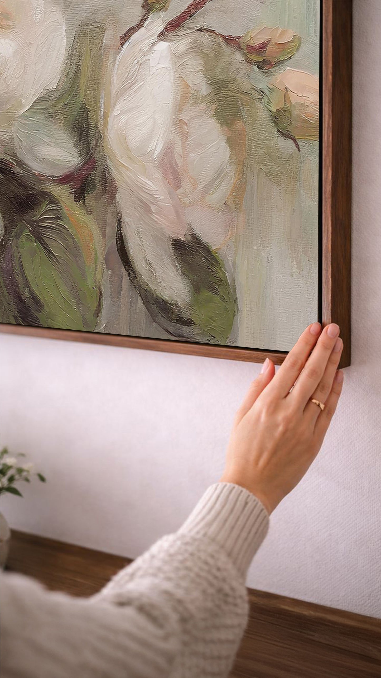 A person's hand is reaching towards a large painting hanging on a wall, which features a floral design with green and white colors.