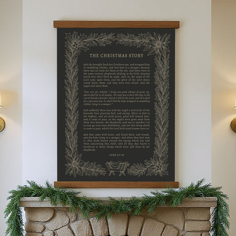 a black framed poster of the Christmas story, hanging on a wall above a fireplace decorated with a garland.