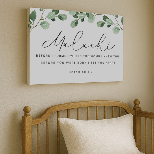 a wooden crib with a white pillow on it, and above it is a framed Bible verse with a green leaf design.