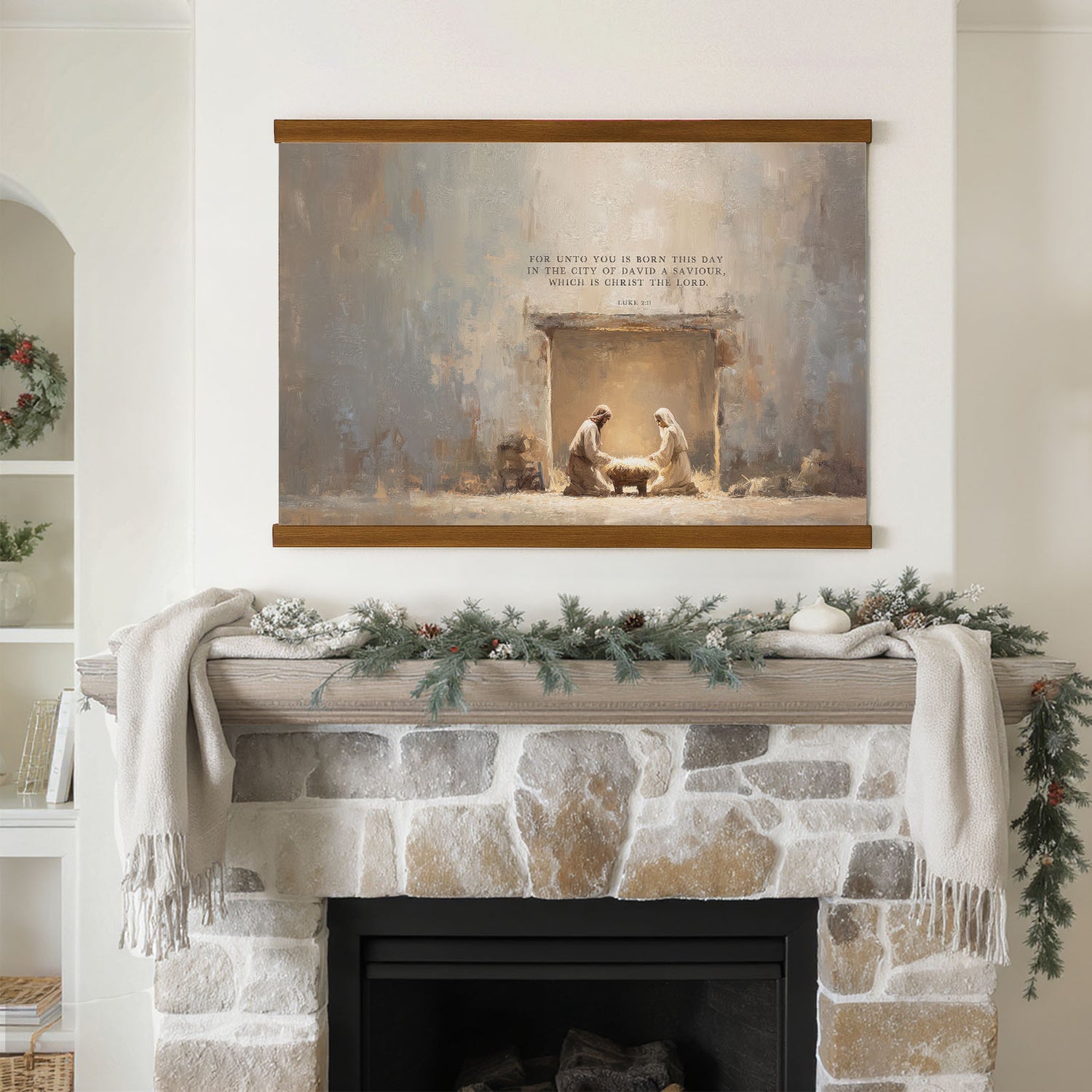 a fireplace mantel decorated with a Christmas wreath, pine cones, and a white candle. Above the mantel is a framed painting depicting a nativity scene with two figures, likely representing Mary and Joseph, in a room with a stone fireplace.