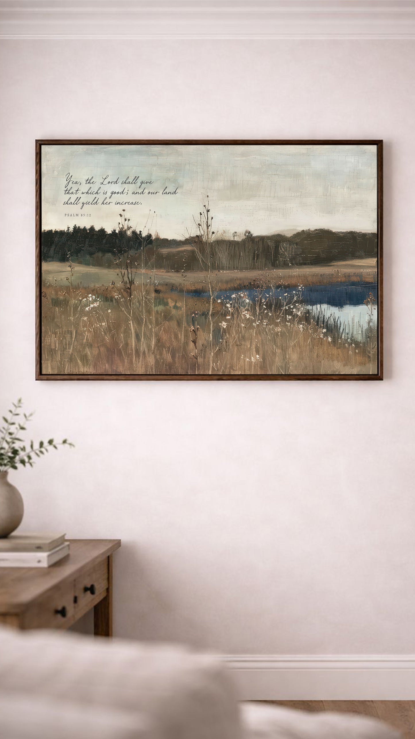 a painting of a serene landscape with a lake, trees, and a field, hanging on a wall above a wooden table with a vase of flowers.