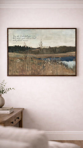 a painting of a serene landscape with a lake, trees, and a field, hanging on a wall above a wooden table with a vase of flowers.