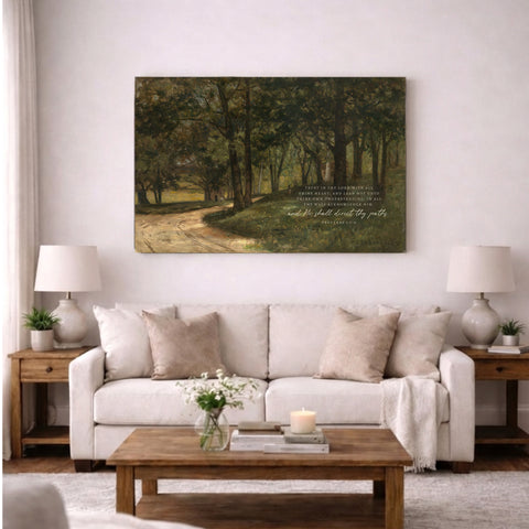 a cozy living room with a large painting of a forest scene hanging on the wall above a white sofa. The sofa is adorned with throw pillows and a blanket, creating a comfortable and inviting atmosphere. A wooden coffee table sits in front of the sofa, and a lamp is placed on a side table. The room is decorated with a vase of flowers and a book, adding a touch of elegance and warmth to the space.