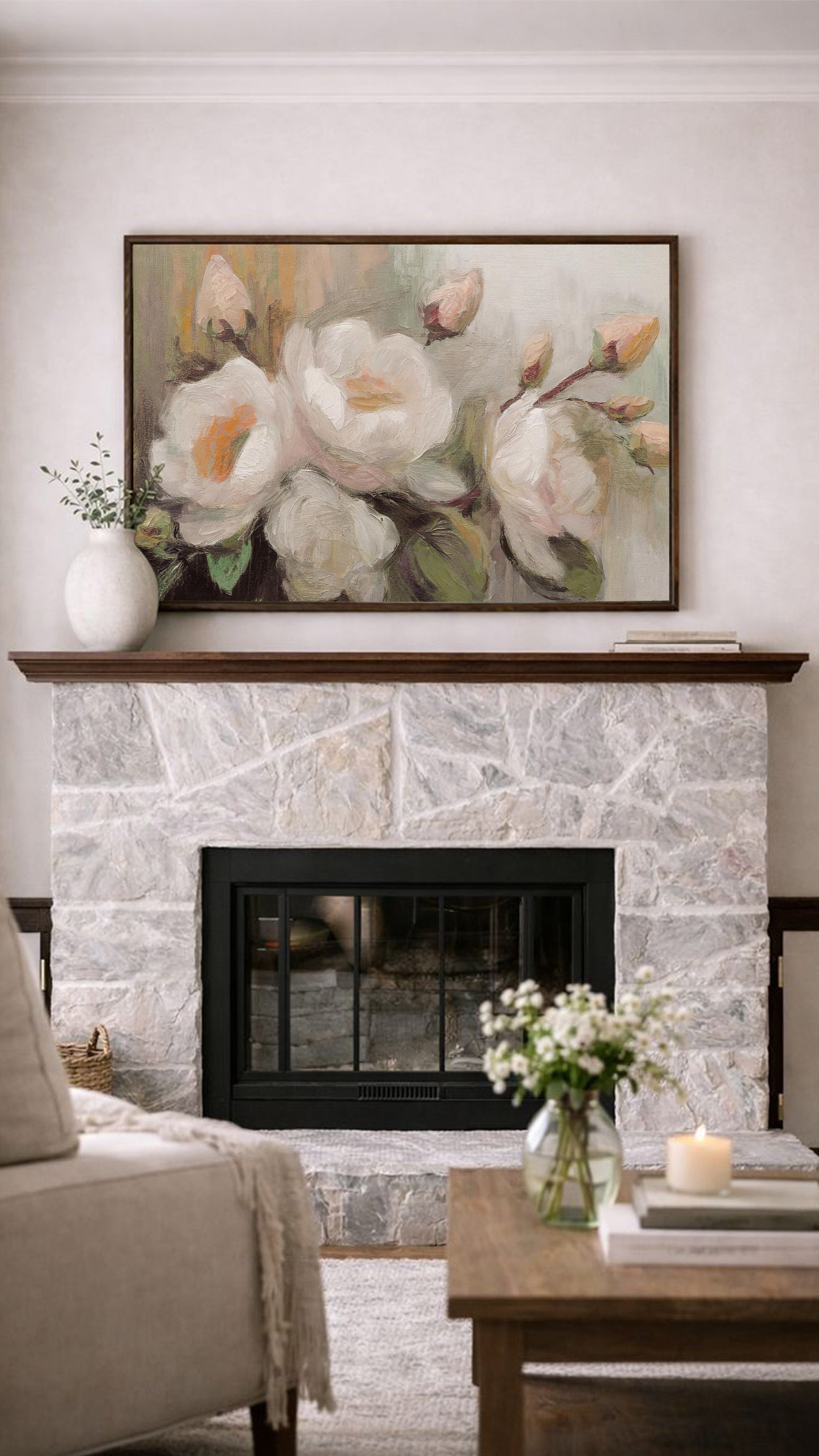 a cozy living room with a stone fireplace, a wooden coffee table, and a framed painting of white flowers above the fireplace.