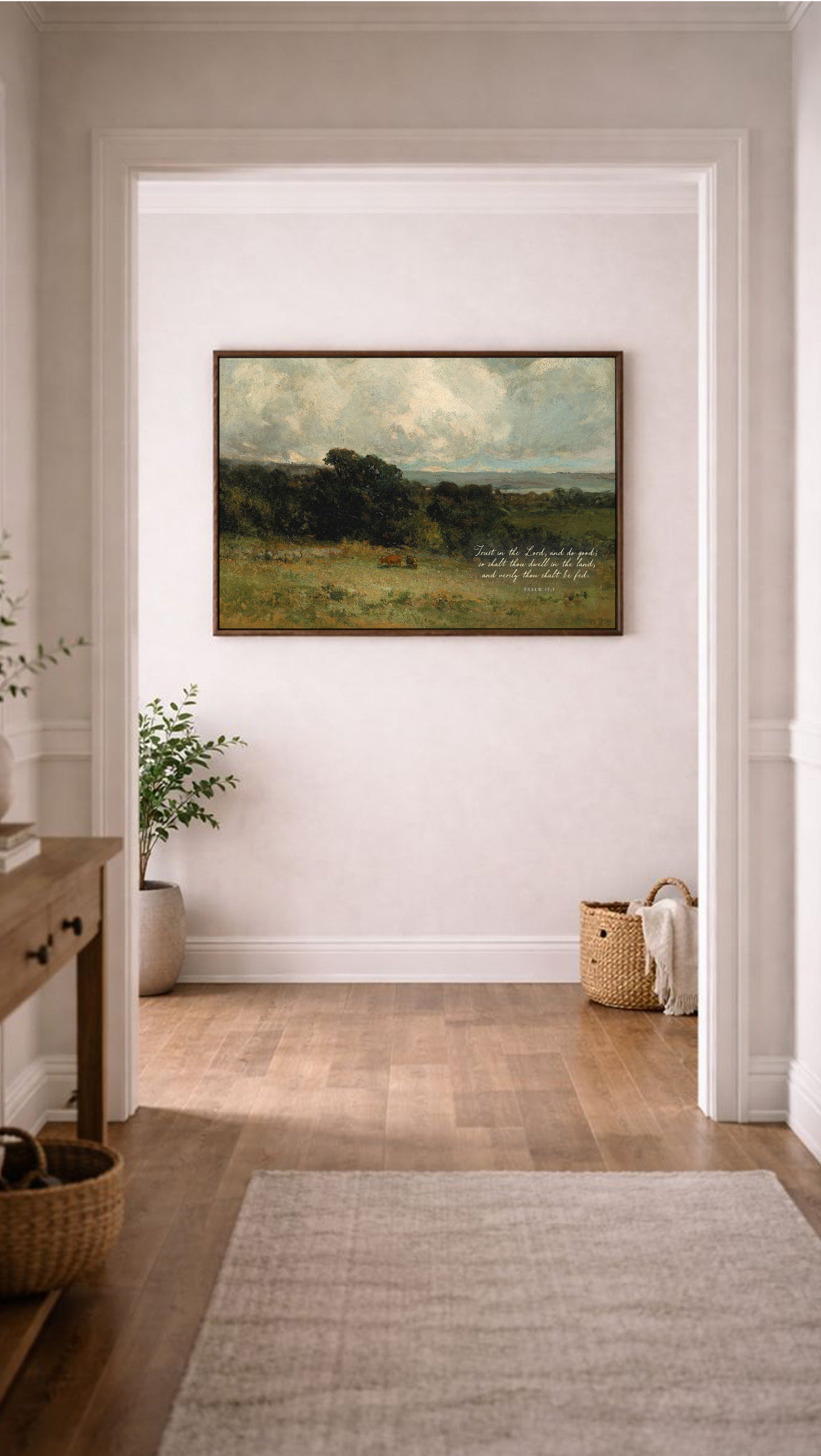 a large landscape painting hanging on a white wall in a hallway. The painting depicts a serene countryside scene with rolling hills, trees, and a cloudy sky. The hallway has a wooden floor and a rug, and there are baskets and a plant visible in the background.