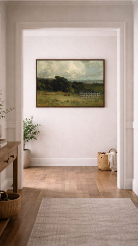 a large landscape painting hanging on a white wall in a hallway. The painting depicts a serene countryside scene with rolling hills, trees, and a cloudy sky. The hallway has a wooden floor and a rug, and there are baskets and a plant visible in the background.