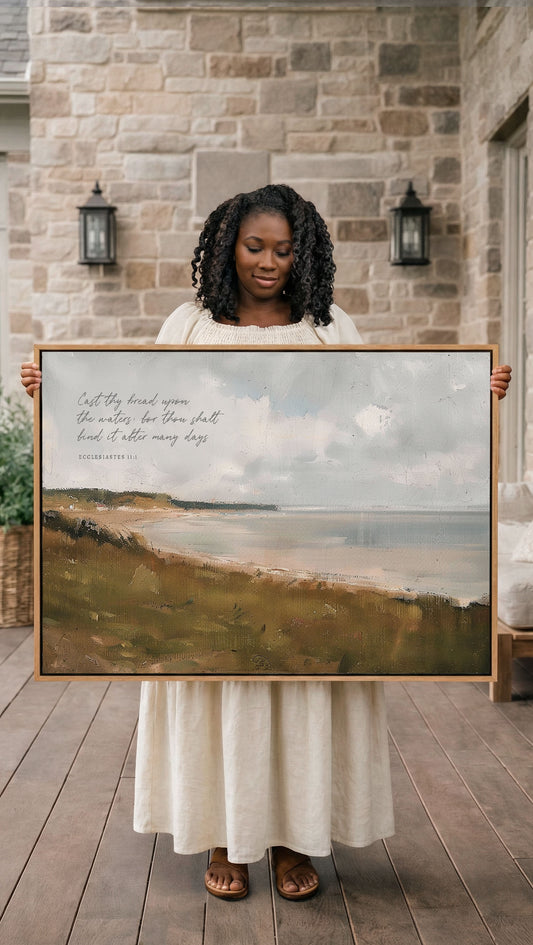 A woman in a white dress holds a large painting of a serene landscape, including a body of water and a sky with clouds, in front of a stone wall.