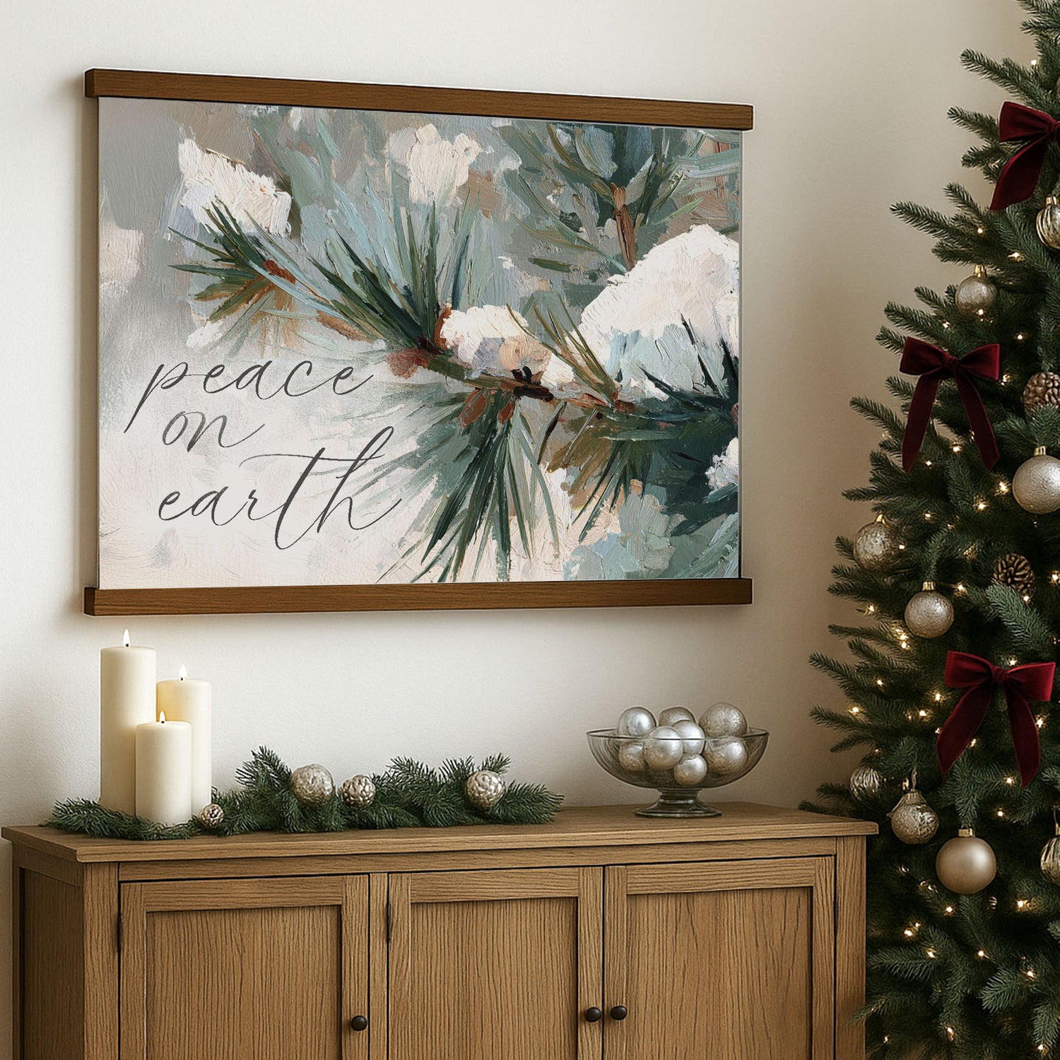 a wooden cabinet with a framed painting of pine branches and greenery hanging above it, along with a bowl of silver ornaments and candles on the cabinet.