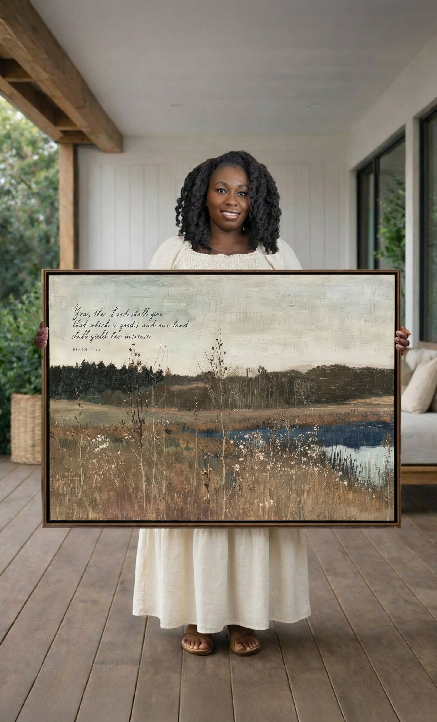 A woman in a white dress holds a large painting of a serene landscape with a lake and trees, standing on a wooden porch.