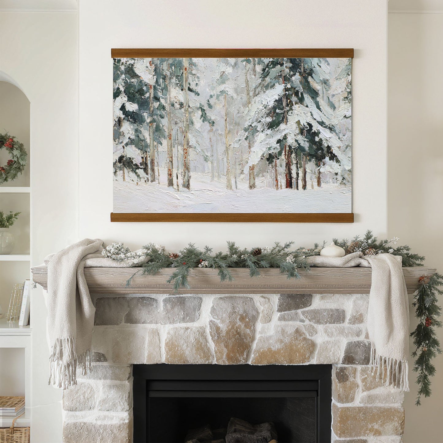 a cozy fireplace adorned with a wreath and a blanket, with a framed painting of a snowy forest hanging above it.