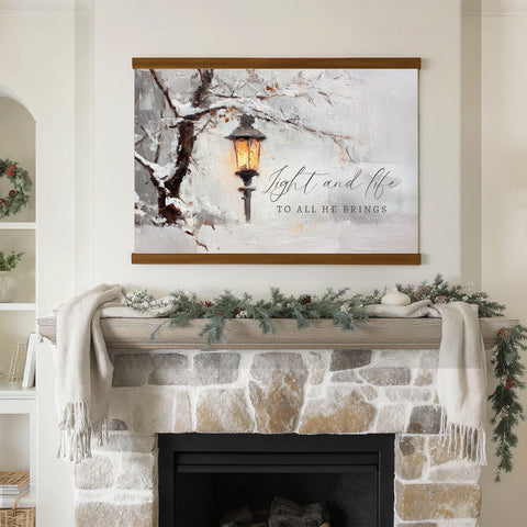 a fireplace mantel decorated with a wreath, pine cones, and a white blanket. Above the mantel is a framed painting depicting a lantern in a snowy landscape.