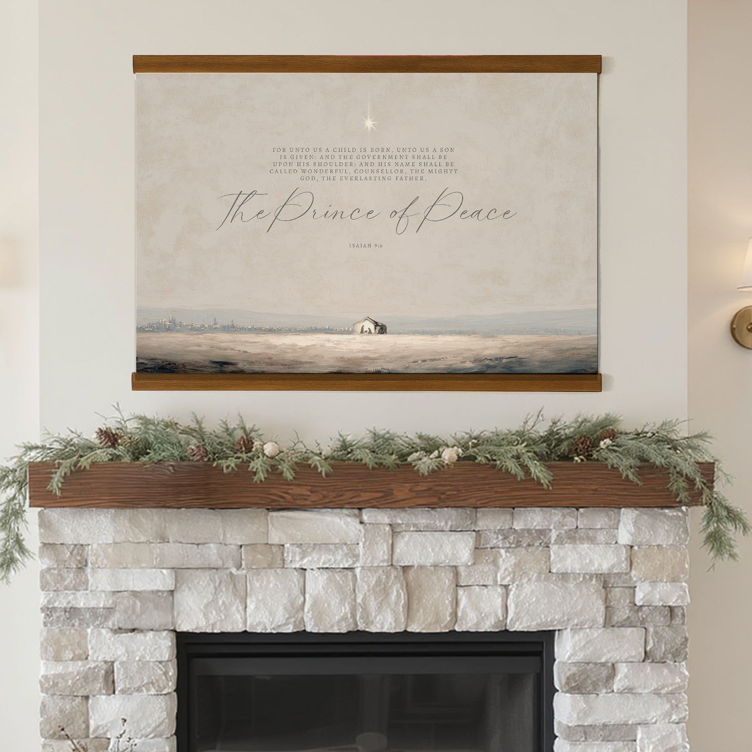 a fireplace with a framed painting of a landscape above it, decorated with greenery and pine cones.