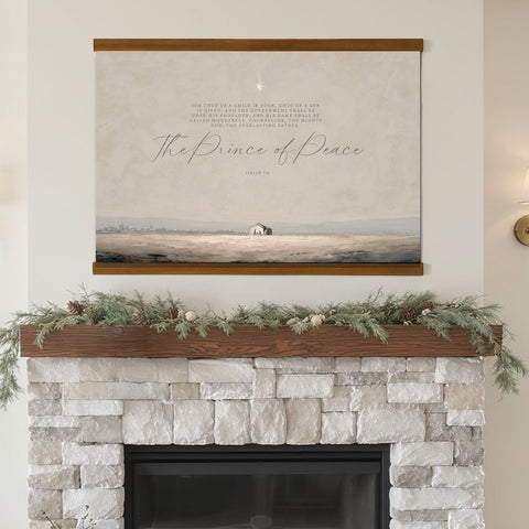 a fireplace with a framed painting of a landscape above it, decorated with greenery and pine cones.