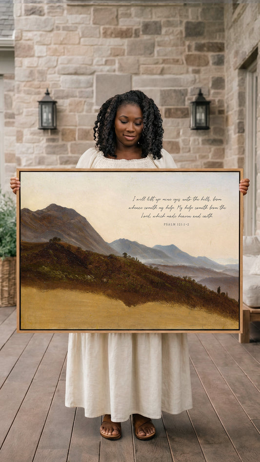 A woman in a white dress holds up a framed painting of a mountainous landscape, with a Bible verse visible in the image.