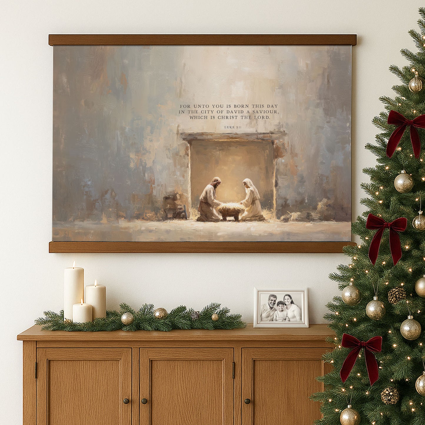 a large painting of the Nativity scene, with two figures of Mary and Joseph in the manger, surrounded by a baby. The painting is hung on a wall above a wooden cabinet, which has a framed photograph and some candles on it. To the right of the painting, there is a Christmas tree decorated with ornaments and ribbons.