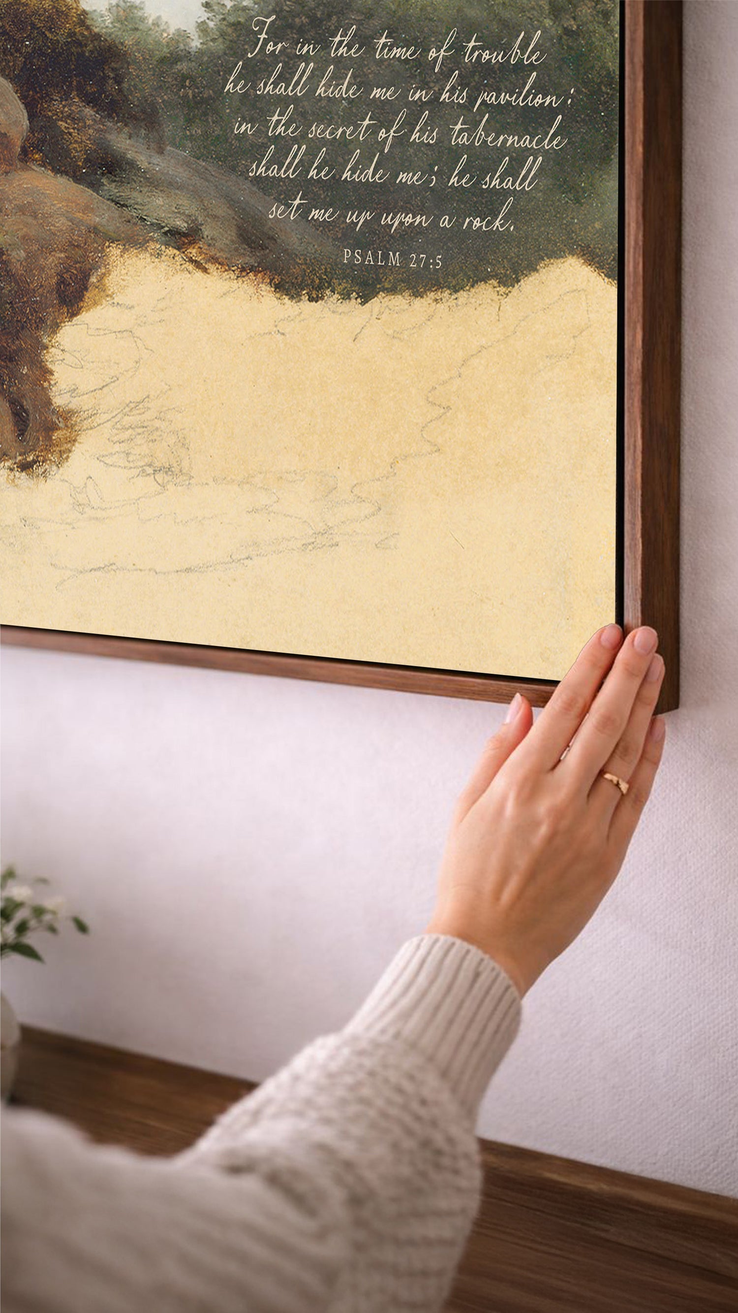A person's hand is reaching up towards a framed painting on a wall, with a Bible verse visible in the painting.