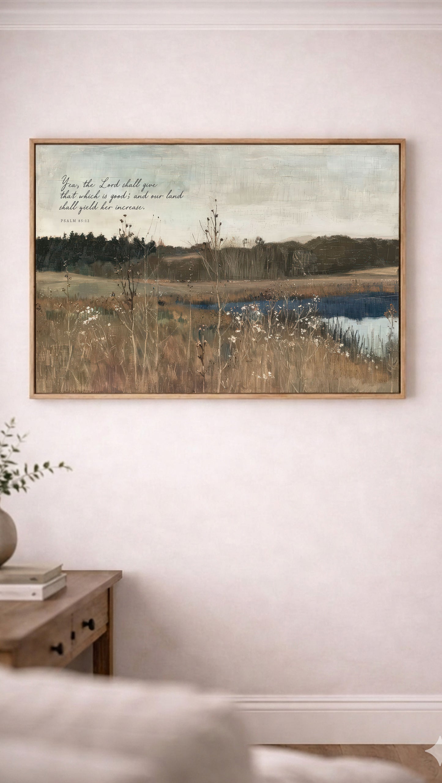 a painting of a serene landscape with a body of water, trees, and a field of tall grass. The painting is hung on a wall above a wooden table with a plant on it.