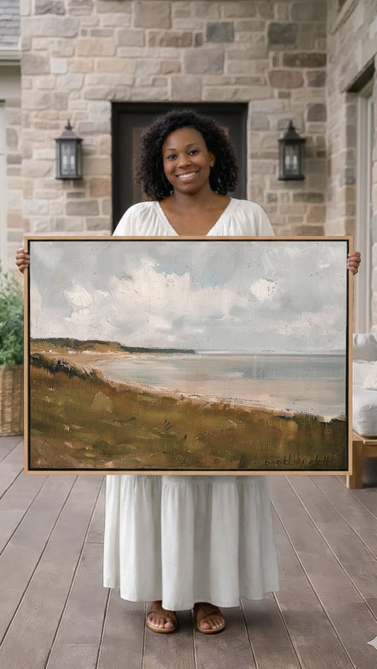 A woman in a white dress holds up a large painting of a landscape, displaying the artwork in front of a stone building.