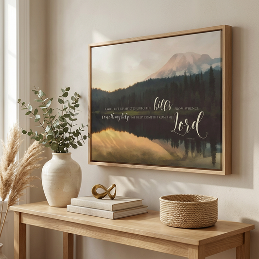 a wooden console table with a white vase, a stack of books, and a woven basket. Above the table, there is a framed print depicting a mountain landscape with a quote from the Bible.