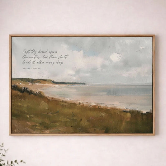 a framed painting of a serene landscape with a body of water and a cloudy sky, hanging on a wall above a wooden table with a plant on it.