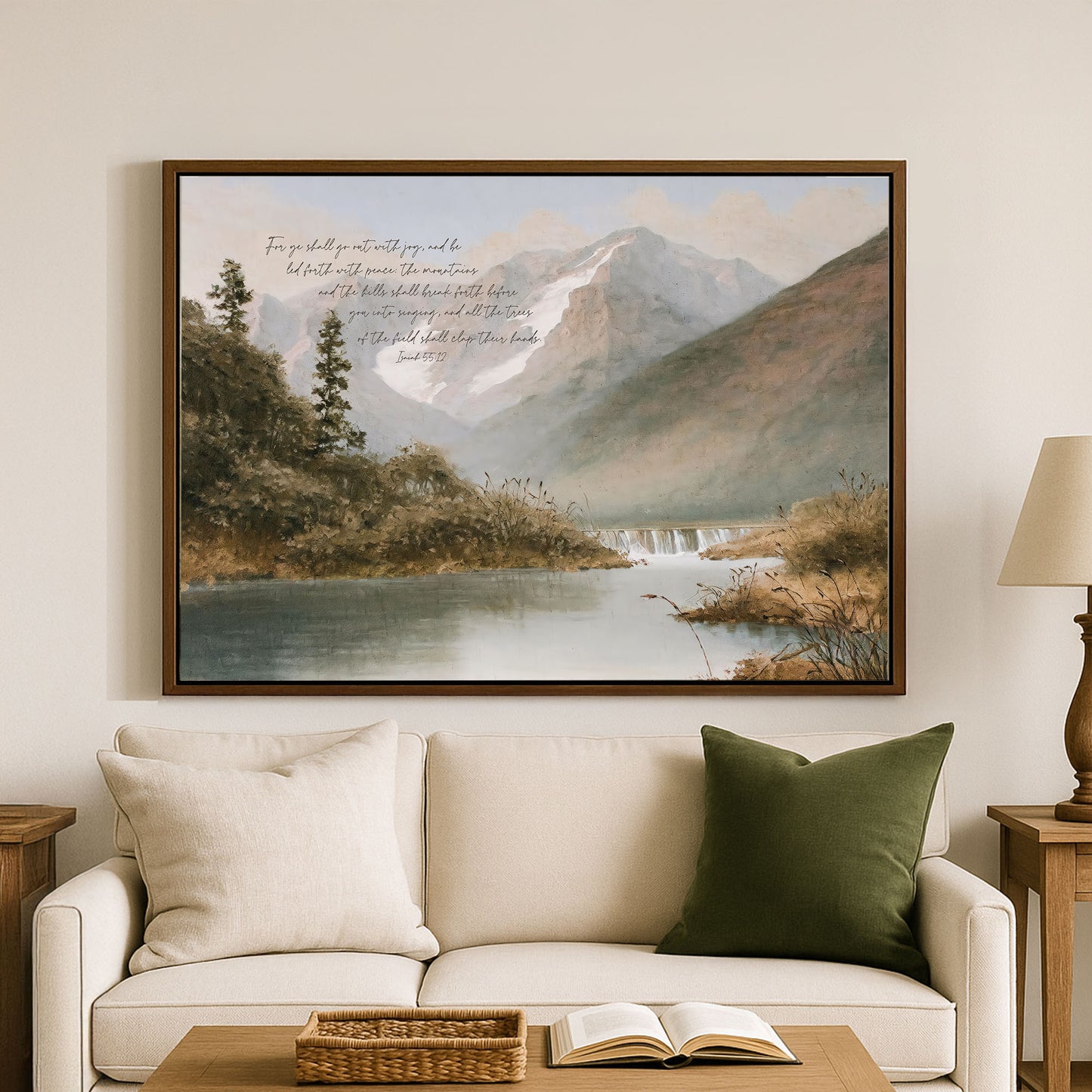 a serene landscape with a mountain range, a river, and lush greenery. The painting is hung on a wall above a white couch, which has a basket on it. The couch is positioned in front of a coffee table, and there is a lamp on a side table next to the couch.